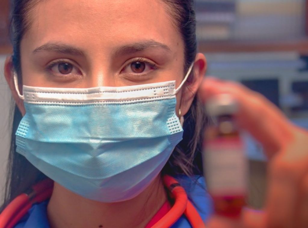 Una funcionaria de salud usa barbijo y sostiene una vacuna. / Foto: MSYD.