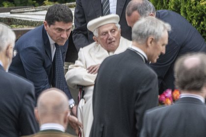El papa emérito Benedicto XVI es auxiliado en su silla de ruedas durante la visita a la tumba de sus padres y hermana en el cementerio Ziegetsdorf, cerca de Ratisbona, Alemania, el sábado 20 de junio de 2020. (Armin Weigel/dpa vía AP)