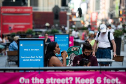 Una mujer con una máscara protectora bebe una taza de café mientras está sentada en una mesa al aire libre en Times Square 