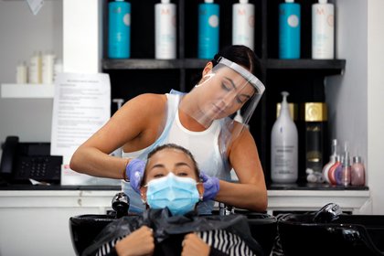 Una peluquera con protector facial lava el pelo de una cliente en Newport Pagnell, Gran Bretaña, 