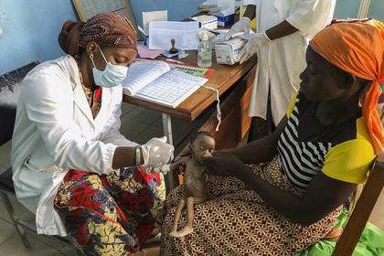 Haboue Solange Boue, de un mes de edad, está sentada en el regazo de su madre Danssanin Lanizou, mientras una enfermera le inserta un goteo intravenoso en el brazo para tratarla por desnutrición grave (AP Photo/Sam Mednick)
