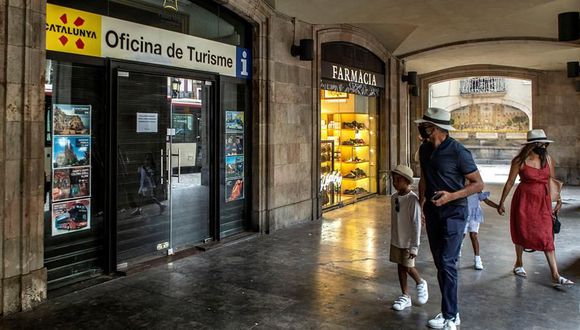 Coronavirus España: Una familia de visitantes camina ante una oficina de turismo cerrada en el centro de Barcelona este martes, cuando el sector turístico catalán se enfrenta a un nuevo parón, tras la leve reactivación que había vivido después de la apertura de fronteras, por las restricciones impuestas por países como Reino Unido a los turistas que vienen de España o las recomendaciones de Francia y Alemania de no viajar a Cataluña. (EFE/Enric Fontcuberta).