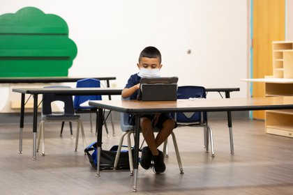Un estudiante asiste a una clase virtual mientras es monitoreado por asistentes de instrucción cuando se reanuda el aprendizaje en una escuela primaria en Phoenix, Arizona (Reuters)