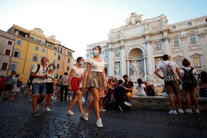 Personas con máscaras faciales caminan frente a la Fontana de Trevi