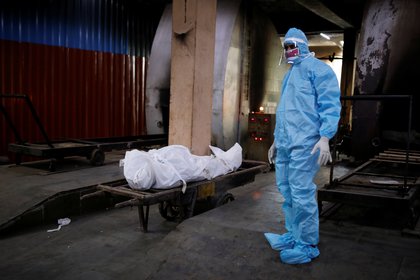Un hombre que lleva equipo de protección personal está de pie junto al cuerpo de un familiar que murió debido a la enfermedad coronavirus (COVID-19), antes de ser cremado en un crematorio en Nueva Delhi, India, el 22 de agosto de 2020. REUTERS/Adnan Abidi