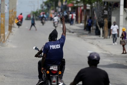 Un manifestante con una camiseta de la policía dispara un arma mientras conduce una moto en las calles de Puerto Príncipe (REUTERS/Andrés Martínez Casares)