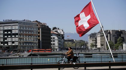 Un ciclista pasa una bandera nacional suiza en un puente de Ginebra (Archivo-Bloomberg)