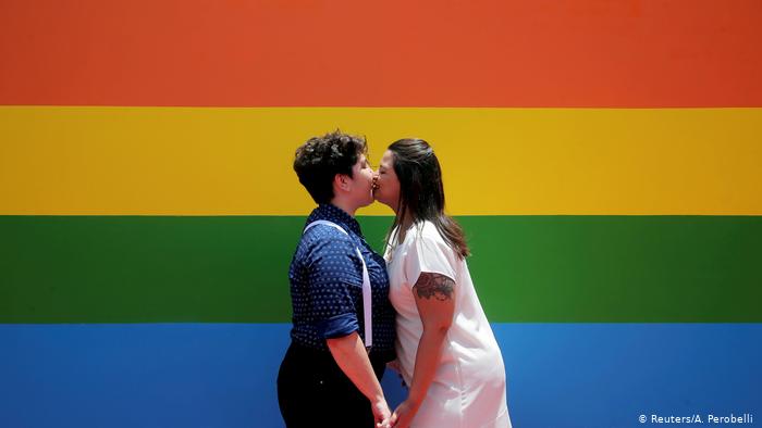 Foto de pareja homosexual frente a la bandera LGBTI