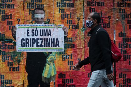 Un ciudadano camina junto a una imagen del presidente Bolsonaro sosteniendo un cartel con su polémico comentario sobre el COVID-19 al inicio de la pandemia (EFE/ FERNANDO BIZERRA/Archivo)
