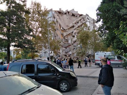 Lugareños observan un edificio dañado después de que un fuerte terremoto golpeó el mar Egeo el viernes y se sintió tanto en Grecia como en Turquía, donde algunos edificios colapsaron en la provincia costera de Izmir, Turquía