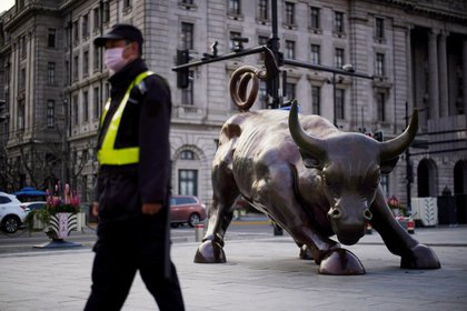 Un guardia de seguridad con una máscara pasa junto a una estatua del toro de Wall Street, luego del brote por la nueva enfermedad por coronavirus (COVID-19), en Shanghai, China. 18 de marzo de 2020. REUTERS/Aly Song