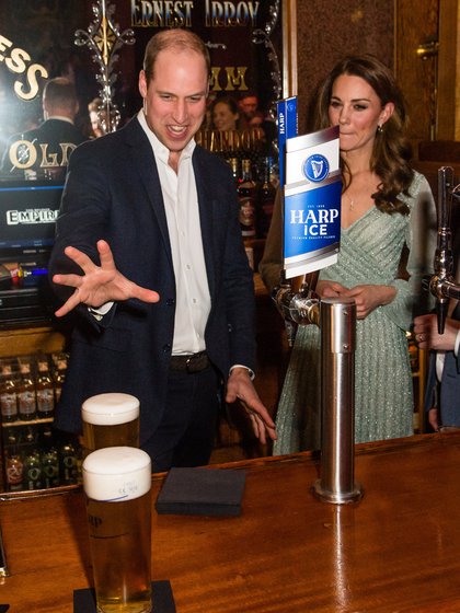 Kate, duquesa de Cambridge, observa al príncipe William quien parece abalanzarse sobre pinta de cerveza durante una visita al Empire Music Hall, Belfast, Irlanda del Norte, en febrero de 2019. Un medio norteamericano publicó que el príncipe estaría bebiendo más de lo recomendable para escapar a sus problemas (Reuters)