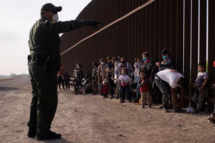 Un agente de la Patrulla Fronteriza de EEUU instruye a los migrantes solicitantes de asilo mientras se alinean a lo largo del muro fronterizo después de cruzar el río Grande hacia Estados Unidos desde México en una balsa, en Penitas, Texas, EEUU. 17 de marzo de 2021. REUTERS/Adrees Latif
