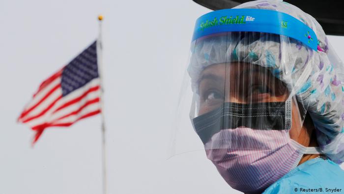 Foto simbólica de una persona trabajadora de Salud con mascarilla frente a una bandera de Estados Unidos.