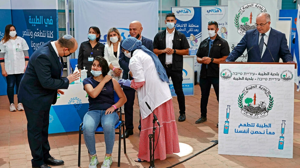 El primer ministro israelí, Naftali Bennett, habla con una joven mientras recibe una vacuna durante contra el covid-19 en una escuela secundaria de la ciudad de Taibeh, Israel, el 19 de agosto de 2021