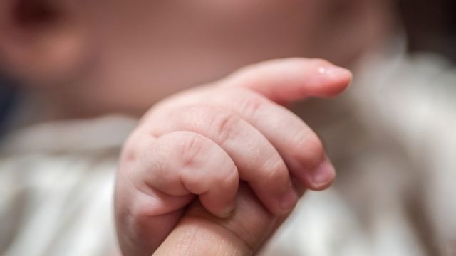 Un bebé toma el dedo índice de un adulto
