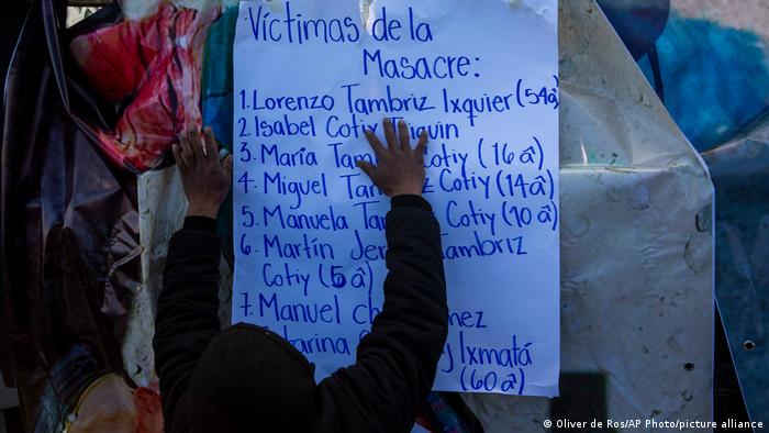 Foto de una persona que sostiene un cartel con los nombres de las víctimas de la masacre de Santa Catarina Ixtahuacan.