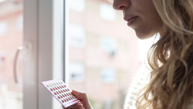 Una mujer sosteniendo pastillas anticonceptivas