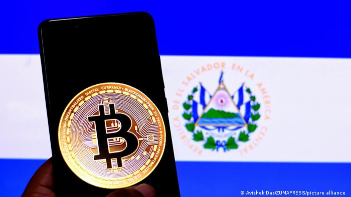 Foto del logo de Bitcoin en una pantalla de celular con la bandera de El Salvador de fondo.