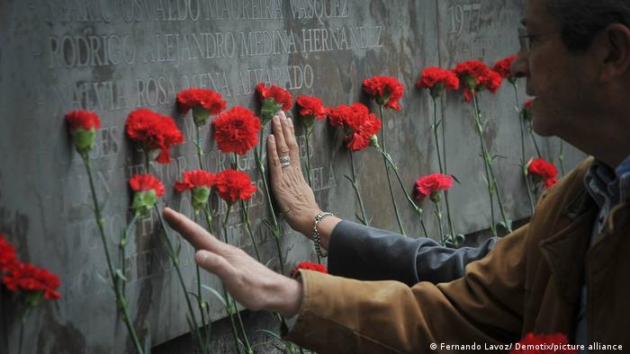 Foto de personas que colocan flores a la par de los nombres de las víctimas de la dictadura de Augusto Pinochet en Villa Grimaldi.