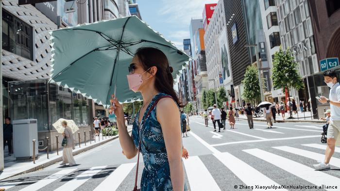Mujer camina por la calle y se protege del sol con un paraguas.
