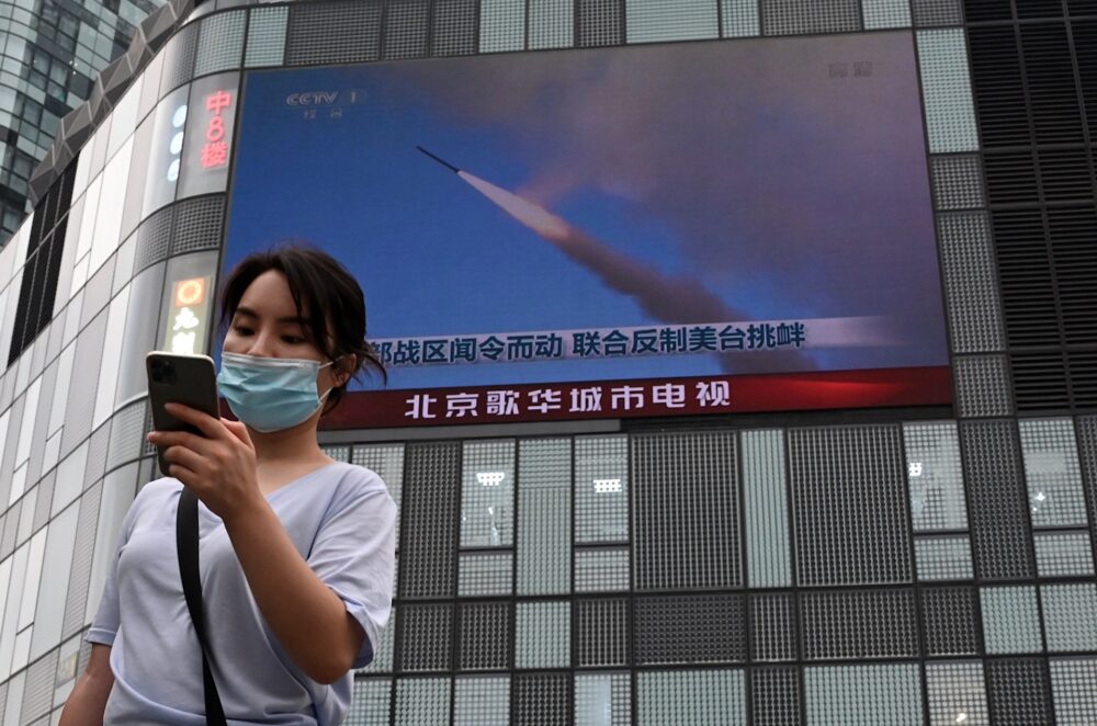 Una mujer utiliza su teléfono móvil mientras camina frente a una gran pantalla que muestra un informativo sobre los ejercicios militares de China que rodean a Taiwán, en Beijing el 4 de agosto de 2022 (Noel Celis / AFP)