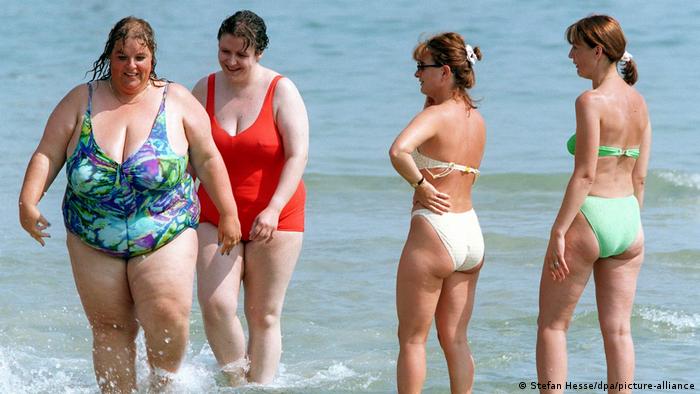 2 mujeres con sobrepeso salen del mar y son observadas por otras 2 mujeres. 