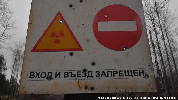 El símbolo de peligro nuclear con una señal de prohibido el país, junto a un cartel en cirílico y con visibles agujeros de bala.