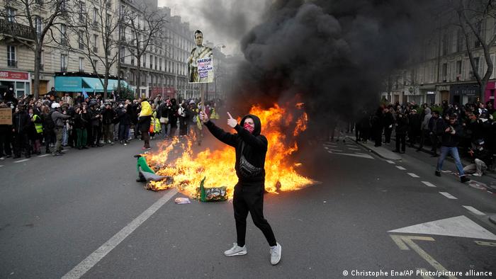 Un manifestante sostiene un cartel burlándose del presidente francés Emmanuel Macron junto a cubos de basura ardiendo durante una manifestación en París. 