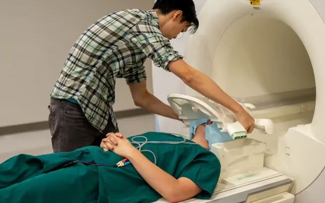 El estudiante Jerry Tang prepara al paciente para recopilar datos de su actividad cerebral dentro del resonador magnético (Nolan Zunk/Universidad de Texas en Austin)
