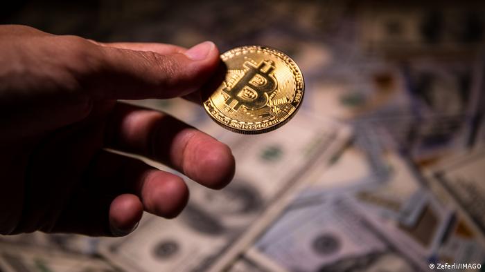 Foto simbólica de una persona que sostiene una moneda con el logo de Bitcoin sobre unos billetes de dólares en una imagen de archivo.