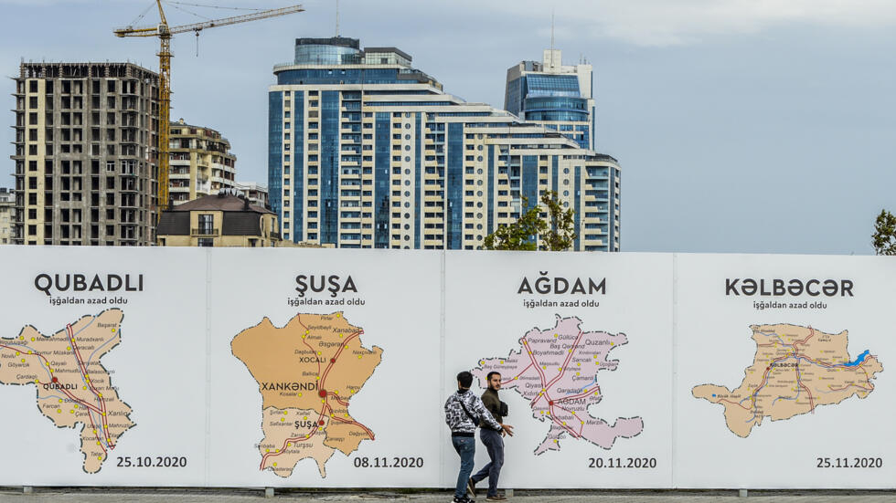 Dos personas pasan delante de unos carteles con mapas de las ciudades de la región de Nagorno-Karabaj, en Bakú, el 13 de septiembre de 2023