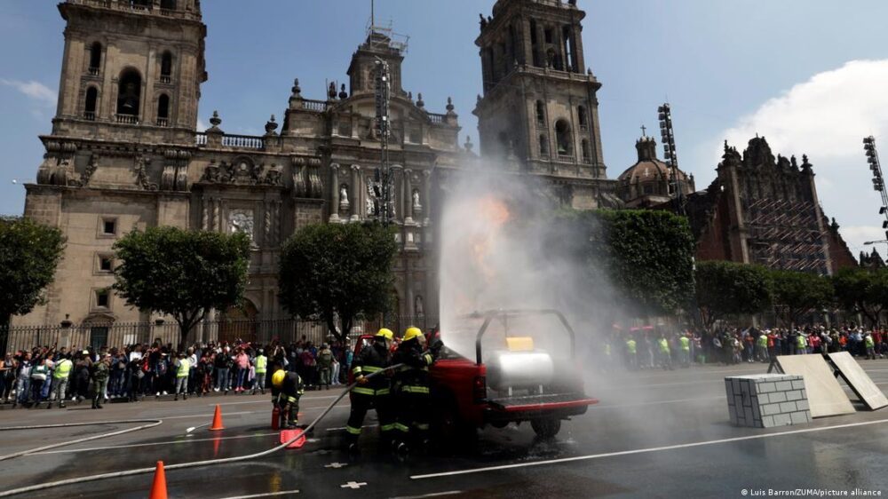 Un grupo de bomberos lanza agua con la catedral al fondo.