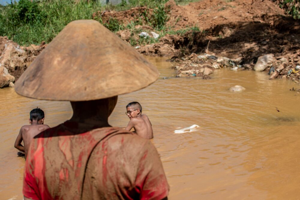 Sentados en charcos de lodo, decenas de menores mueven bateas -bandejas de madera utilizadas en la minería artesanal- entre piedras, vidrio y hasta basura en busca de pepitas de oro que se adhieran al mercurio (Yris PAUL / AFP)