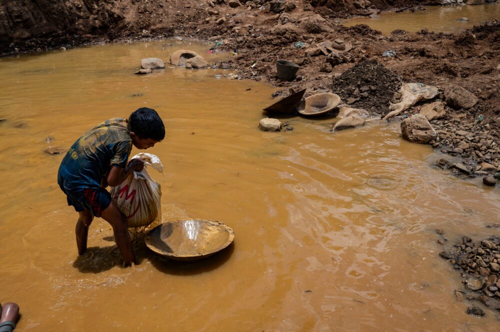 Bajo el sol inclemente y la espalda doblada por el saco que lleva a cuestas, el niño camina como puede hacia otro pozo cercano y sigue su “trabajo” (Magda Gibelli / AFP)