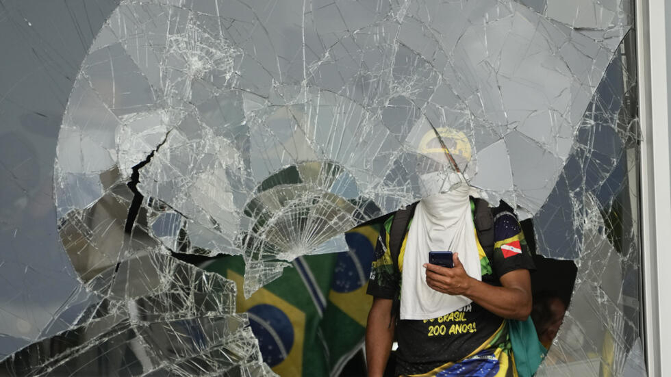 Simpatizantes del expresidente de Brasil Jair Bolsonaro, miran desde una ventana destrozada después de que irrumpieran en el palacio presidencial de Planalto en Brasilia, Brasil, 8 de enero de 2023. Un año después, unas 400 personas siguen encarceladas acusadas de los disturbios y Bolsonaro está siendo investigado por el Tribunal Supremo por su papel en el caos. (AP Photo/Eraldo Peres, Archivo)