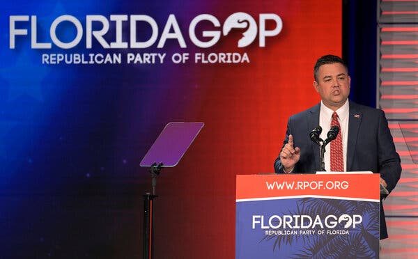 Christian Ziegler viste traje y corbata roja mientras habla en un podio rojo y azul. El logo del Partido Republicano de Florida está en el podio y en una pantalla detrás de él.