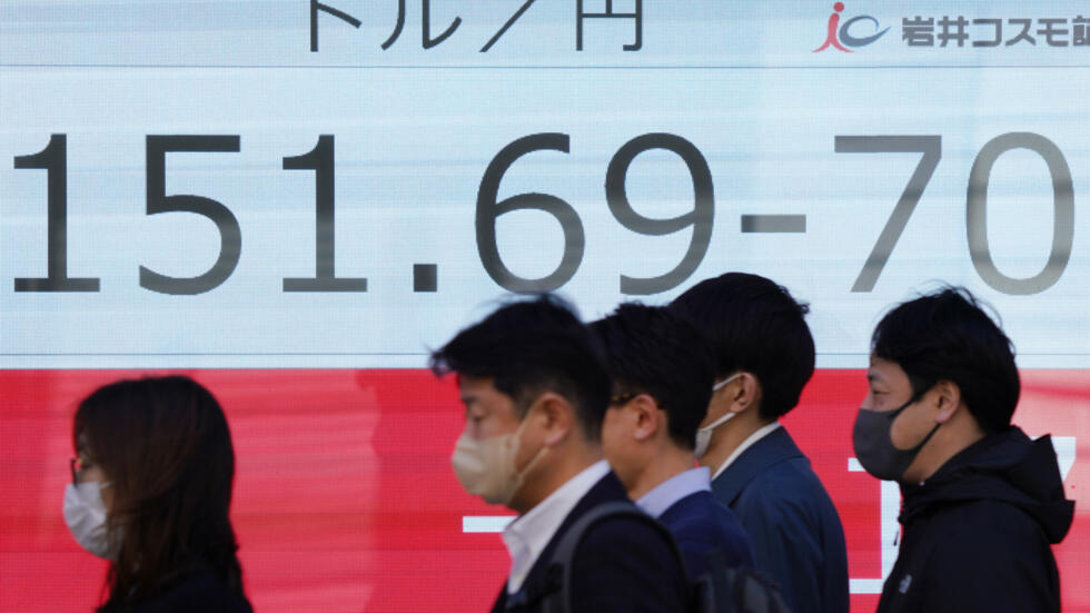 Varios transeúntes pasan frente a un panel electrónico de la cotización del yen japonés frente al dólar, el 27 de marzo de 2024 en una calle de Tokio