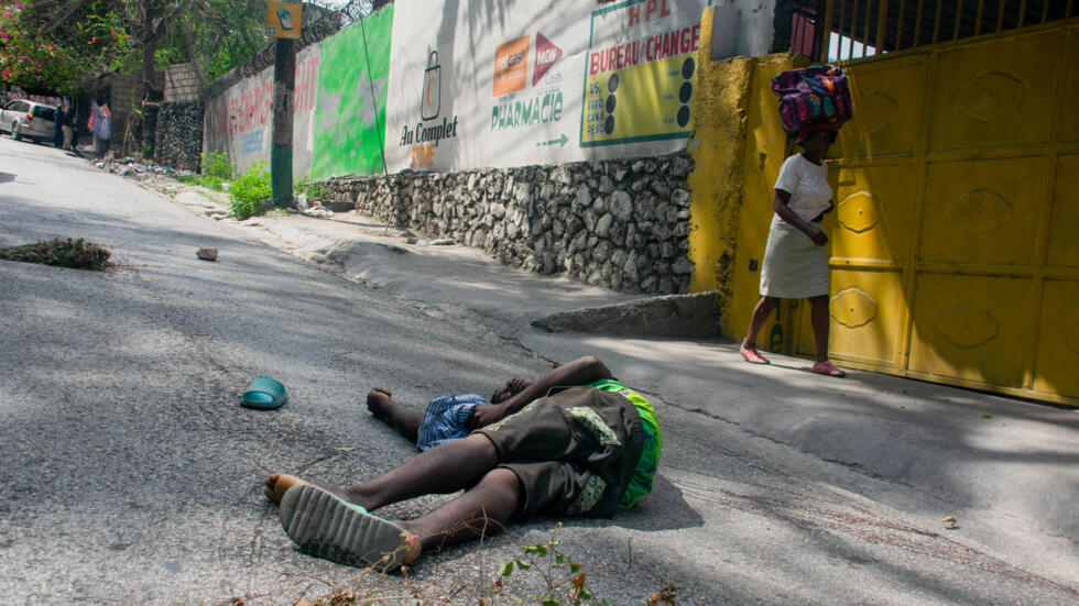 Una mujer pasa junto al cadáver de un hombre abatido por disparos de unos hombres armados sin identificar la noche anterior, el 28 de marzo de 2024 en Puerto Príncipe