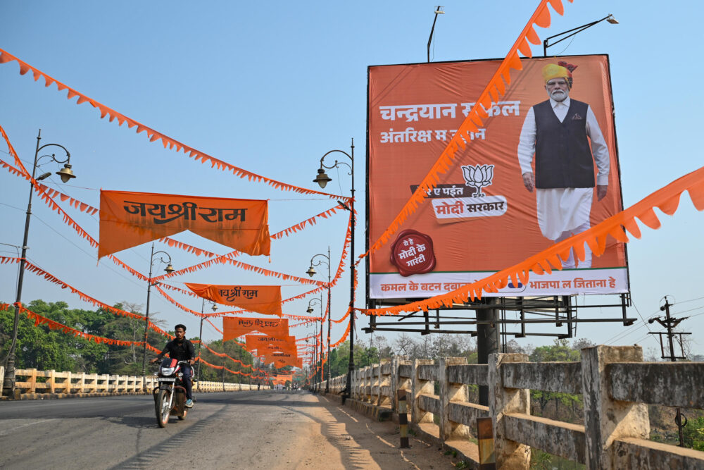 Un hombre circula en moto frente a un cartel electoral del primer ministro Narendra Modi en el estado de Chhattisgarh, en el centro de India, el 16 de abril de 2024