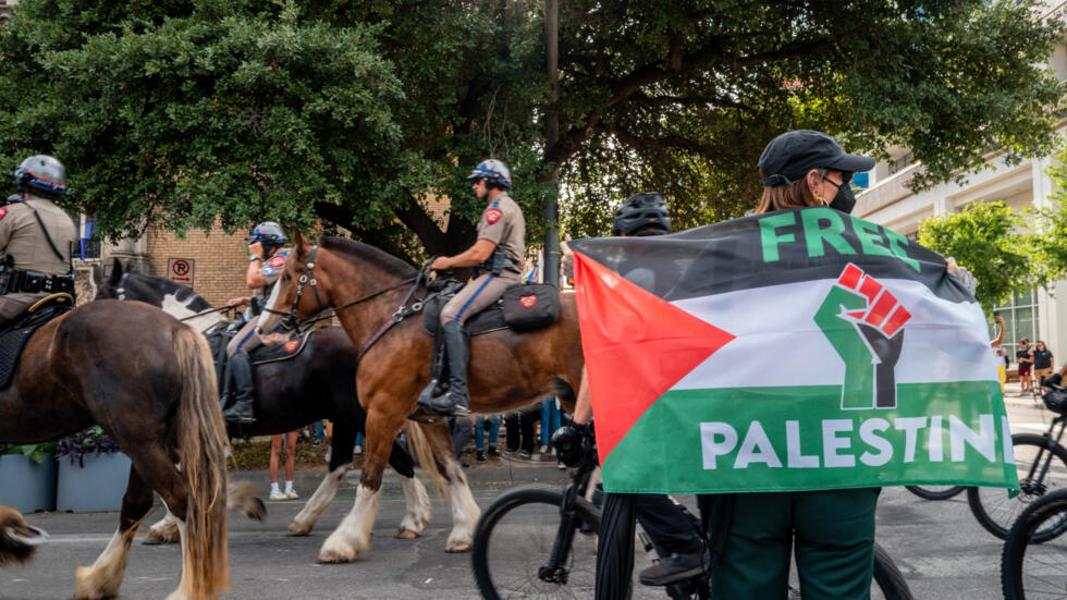 Un hombre exhibe una bandera que dice "Palestina Libre" mientras la policía montada se despliega para contener una protesta por la guerra en la Franja de Gaza en la Universidad de Texas, en Austin (EEUU), el 24 de abril de 2024