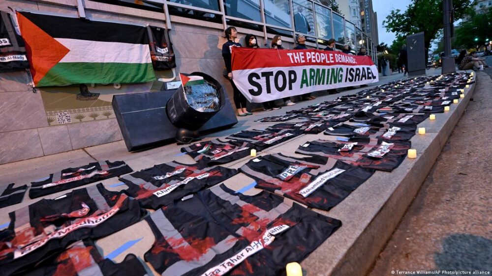 Manifestantes sostienen una pancarta, mientras un chaleco de prensa yace en el suelo cubierto de pintura roja, durante la protesta durante la Cena de la Asociación de Corresponsales de la Casa Blanca, el sábado 27.04.2024.