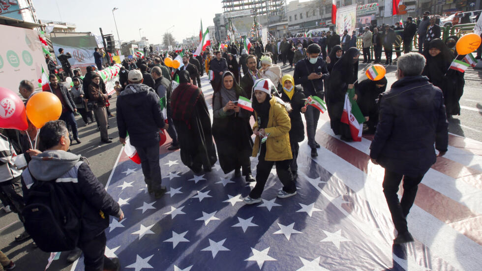 Unos iraníes pisan una gran bandera de Estados Unidos colocada en el suelo en Teherán para conmemorar el 45º aniversario de la Revolución Islámica, el 11 de febrero de 2024