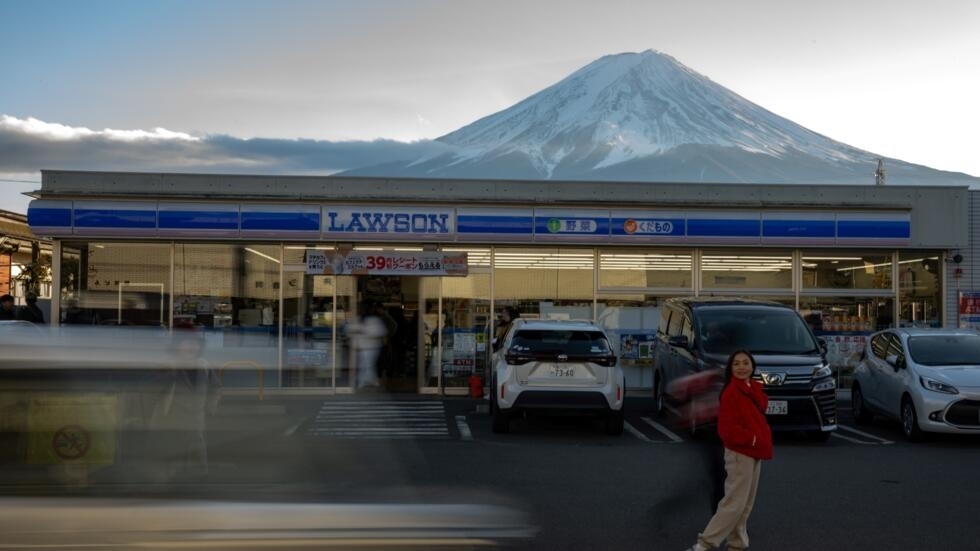 Una turista posa frente a una tienda de conveniencia sobre la que se eleva la silueta del monte Fuji en el pueblo japonés de Fujikawaguchiko, el 1 de enero de 2024