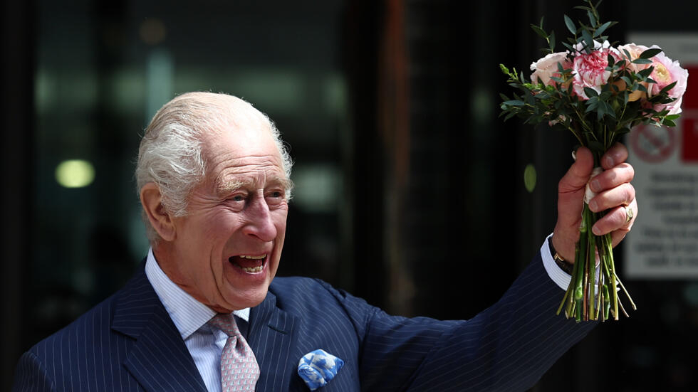El rey Carlos III sonríe con un ramo de flores en la mano al saludar a los curiosos durante una visita a la sección oncológica de un hospital, el 30 de abril de 2024 en Londres