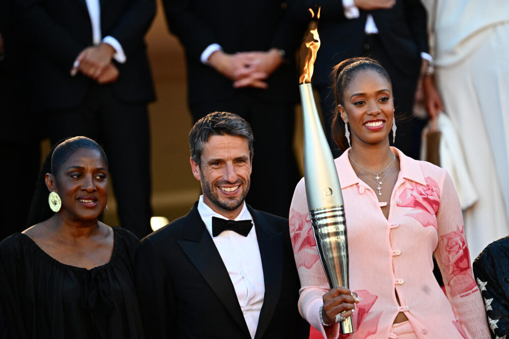 La basquetbolista francesa Iliana Rupert sostiene la llama olímpica junto al presidente del comité organizador de los Juegos de París-2024, Tony Estanguet, y la exatleta francesa Marie-Jose Perec en el Festival de Cannes, el 21 de mayo de 2024