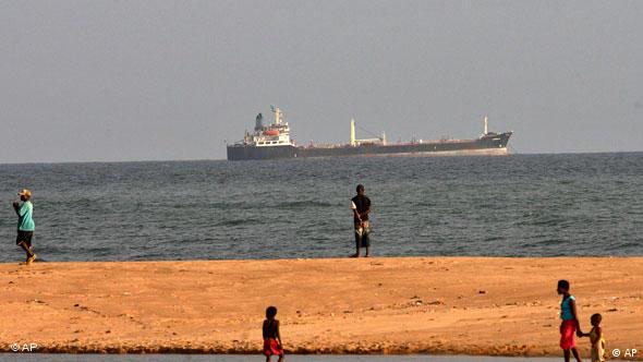 Un buque tanque africano pasa delante de la costa de Benín, mientras algunas personas caminan por la playa.
