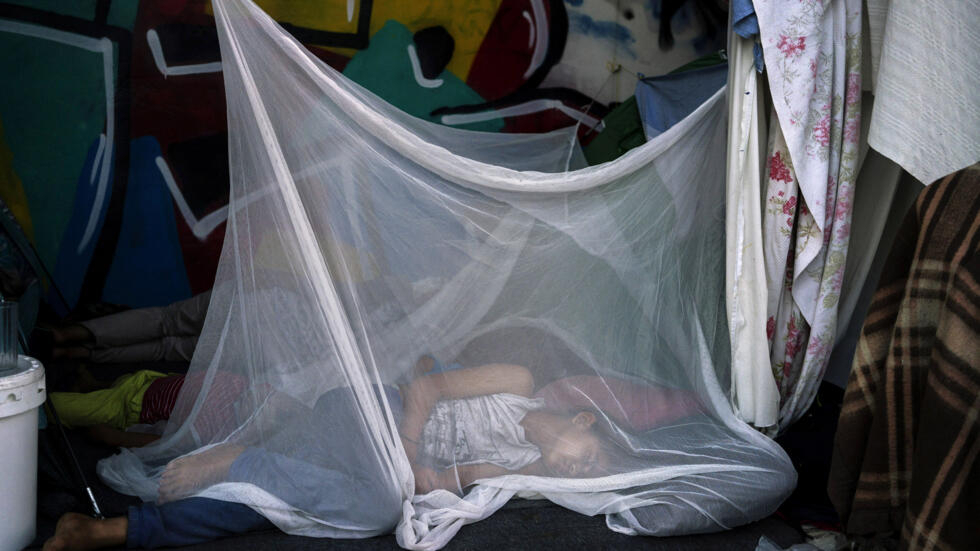 Una niña migrante duerme protegida con una mosquitera el 10 de agosto de 2016 en el antiguo aeropuerto internacional de Atenas, utilizado como campamento temporal