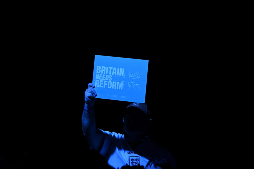Un partidario de la formación de ultraderecha británica Reform UK muestra un cartel con el mensaje "Reino Unido necesita reforma", el 30 de junio de 2024 en Birmingham