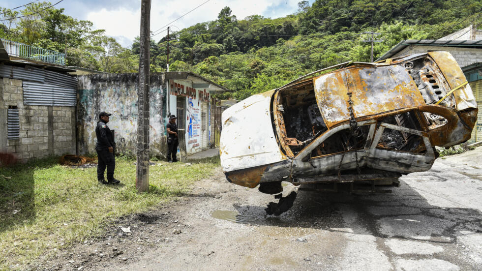 Dos policías observan un vehículo quemado presuntamente por grupos armados que generaron una ola de violencia en Tila, en el estado de Chiapas, el 12 de junio de 2024 al sur de México
